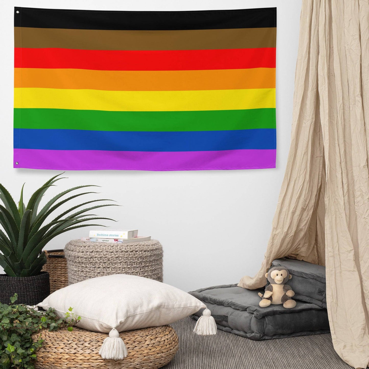 The Philadelphia Pride Flag by Pridelity, featuring horizontal stripes in black, brown, red, orange, yellow, green, blue, and purple, hangs against a white brick wall. This vibrant emblem of diversity and inclusion adds a splash of color reminiscent of a lively rainbow shop.