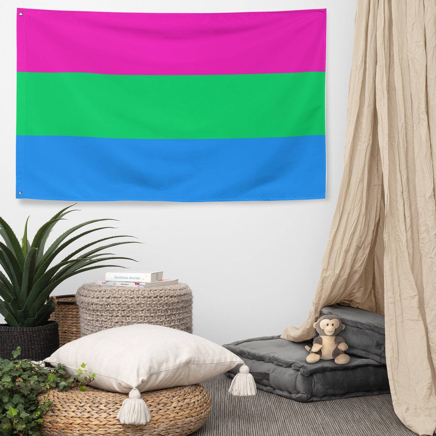 A vibrant Polysexual Flag, featuring three horizontal stripes with pink on top, green in the middle, and blue at the bottom, hangs elegantly on a white brick wall. From Pridelity, it adds a splash of color reminiscent of a rainbow shop display.