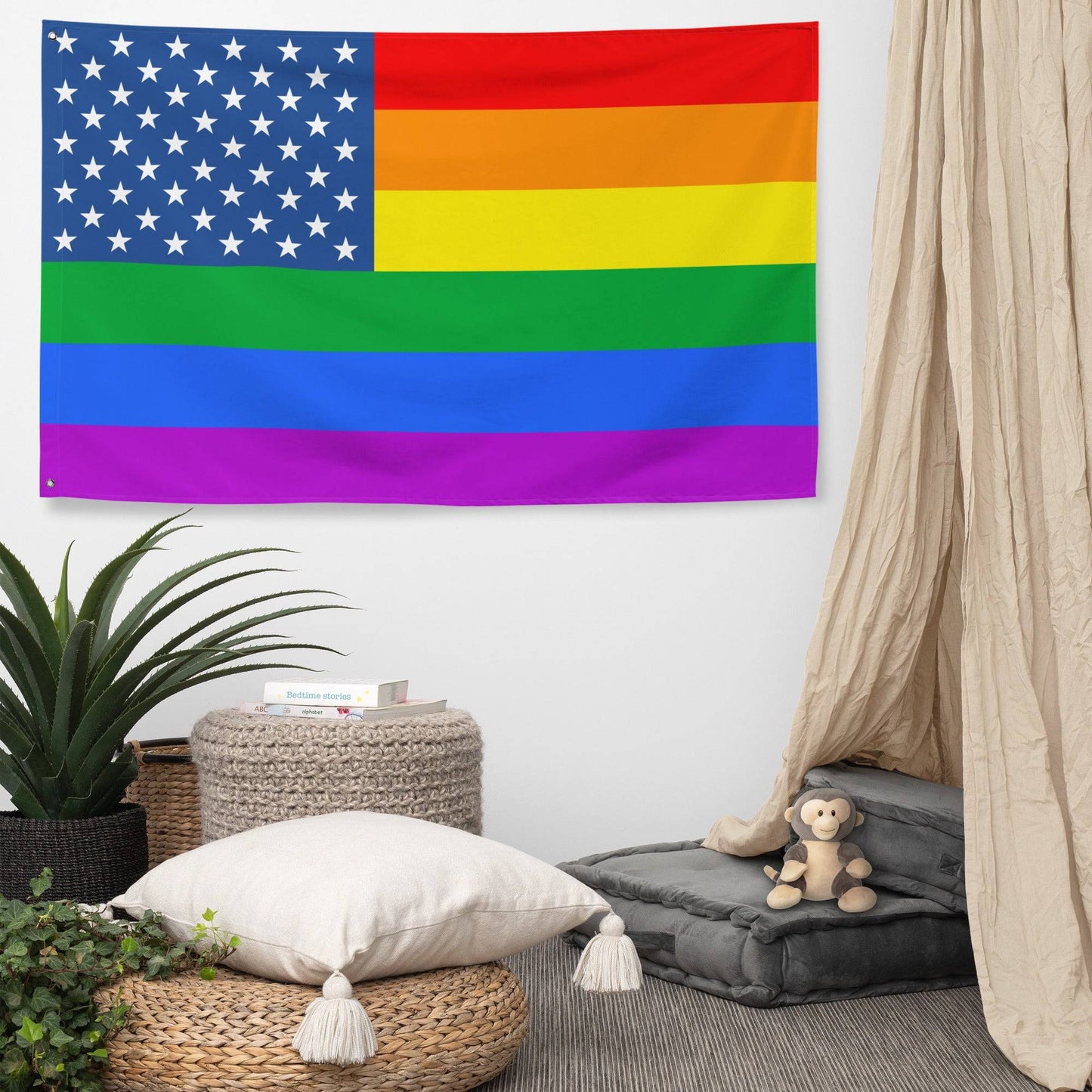 The Pride Stars and Stripes Flag from Pridelity, featuring an American flag seamlessly merged with the vibrant rainbow stripes of the LGBTQ+ pride flag, hangs against a white brick wall. Its stars on a blue background in the top left beautifully contrast with the horizontal rainbow stripes, creating an inviting and colorful display.