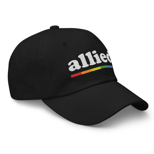 A Pridelity Allied Cap featuring "allied" embroidered in white above a vibrant, Pride-inspired rainbow line.