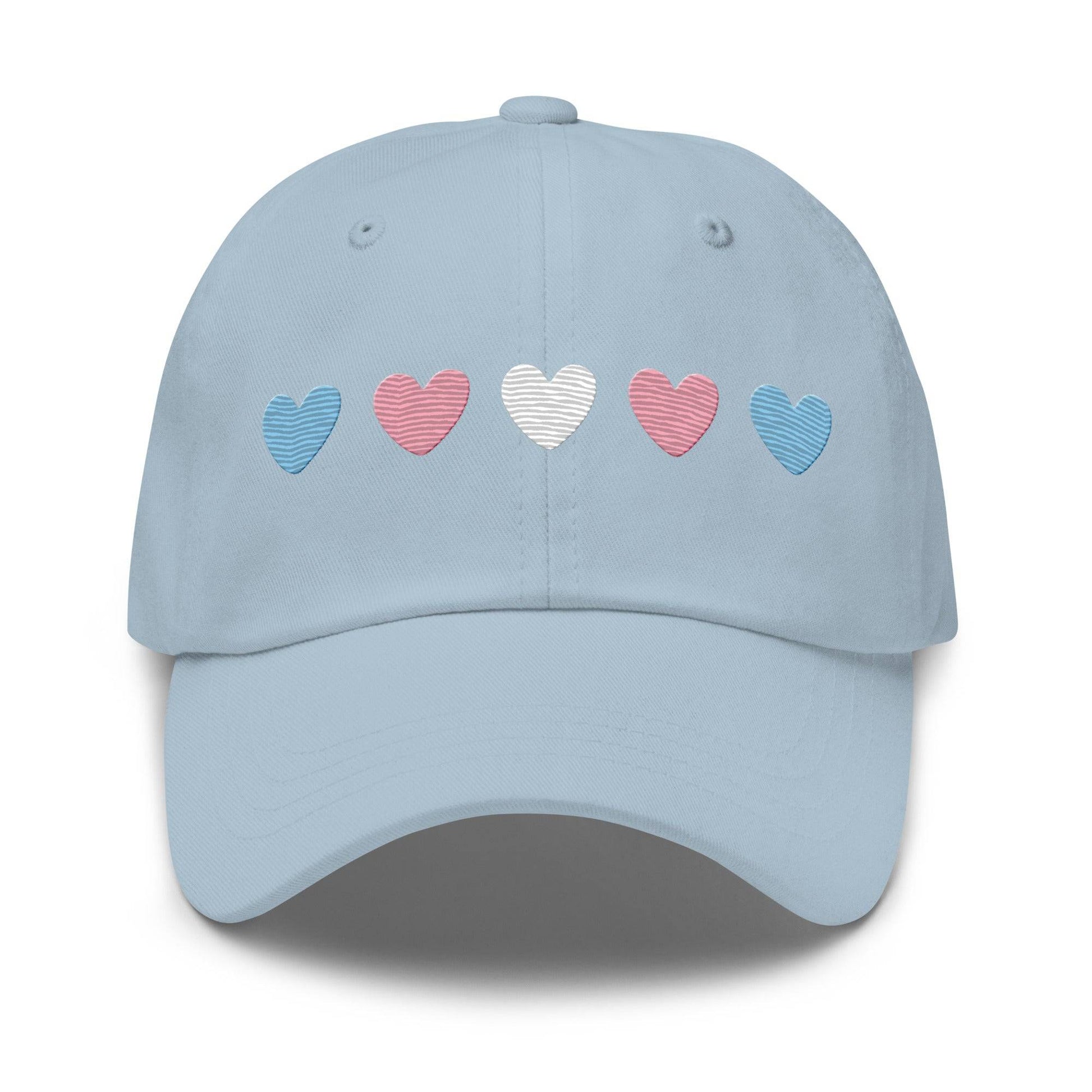 Introducing the "Trans Hearts Cap" from Pridelity, a black baseball cap adorned with embroidered pastel heart designs in pink, white, and blue on the front, making it an ideal accessory to enhance your pride outfits.