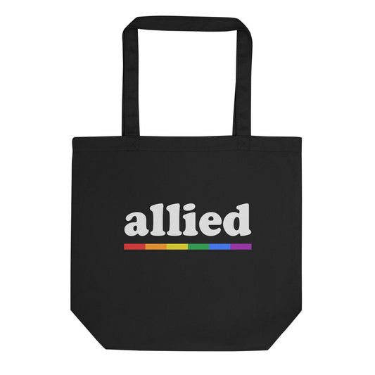 The Pridelity "Allied Tote Bag" is a black tote with long handles, showcasing the word "allied" in white with a horizontal rainbow stripe beneath it, making it a stylish addition to any Pride Collection.