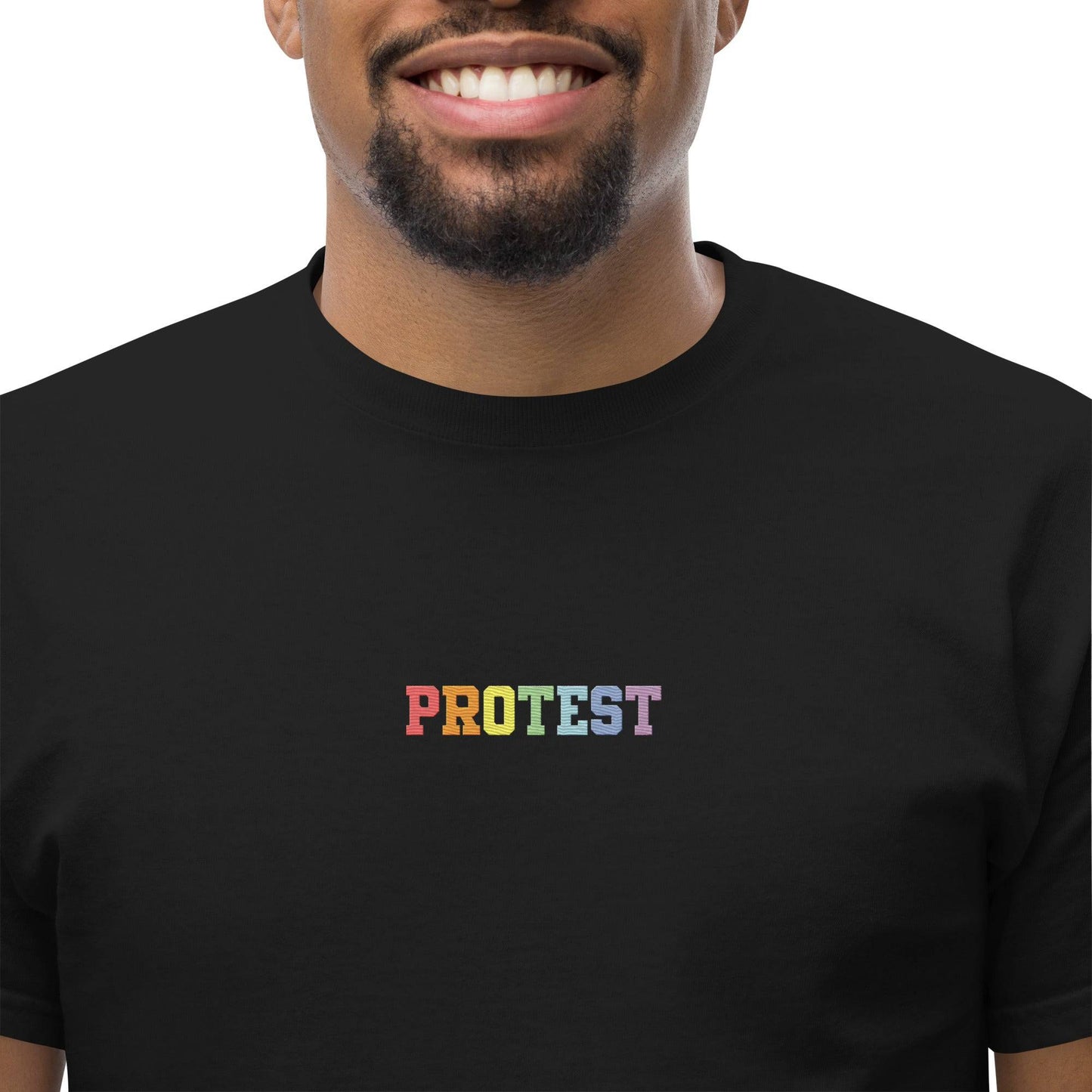 The Protest T-Shirt by Pridelity is a bold black garment featuring the word "PROTEST" displayed prominently in vibrant rainbow-colored letters on the chest, set against a plain white background.
