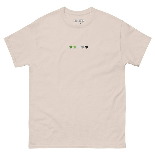 The Aromantic Love T-Shirt by Pridelity is cream-colored and features a row of small hearts across the chest in green, light green, white, gray, and black.