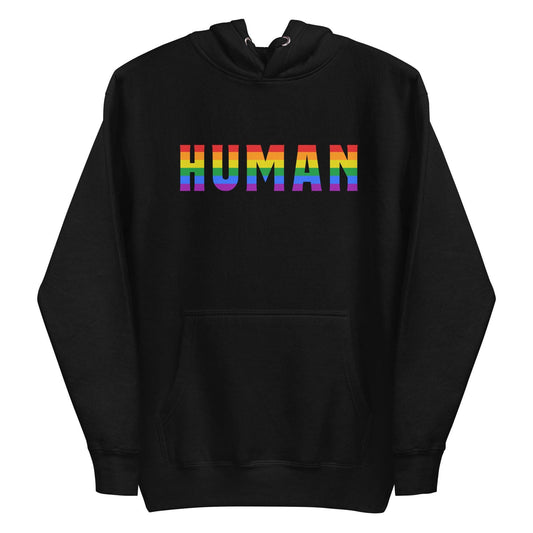 A folded Human Hoodie by Pridelity, featuring the word "HUMAN" prominently displayed in bold, rainbow-colored letters on the front. The black pride hoodie has its hood up, with untied drawstrings resting on the fabric.