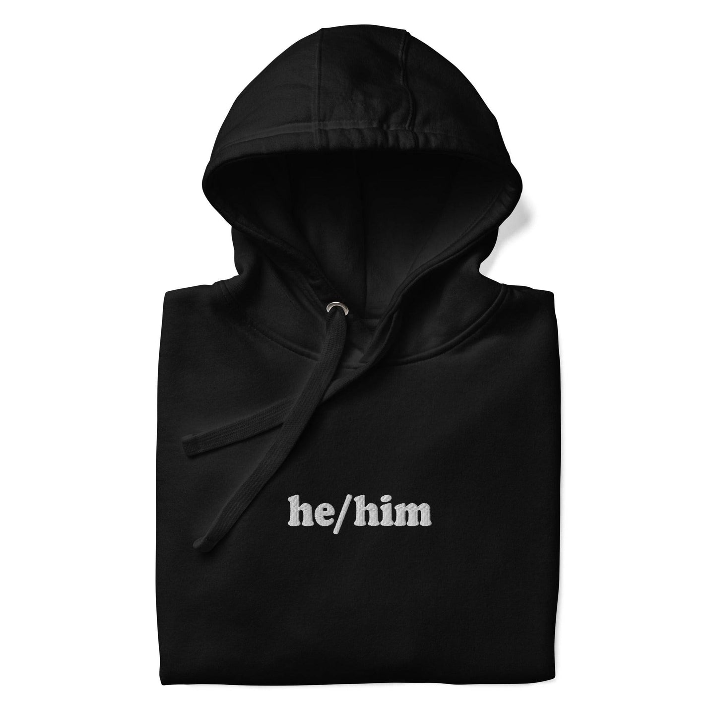 A neatly folded Pridelity He/Him Hoodie in black, featuring the text "he/him" embroidered in white on the front. The hood is showcased with its drawstrings arranged against a plain white background.
