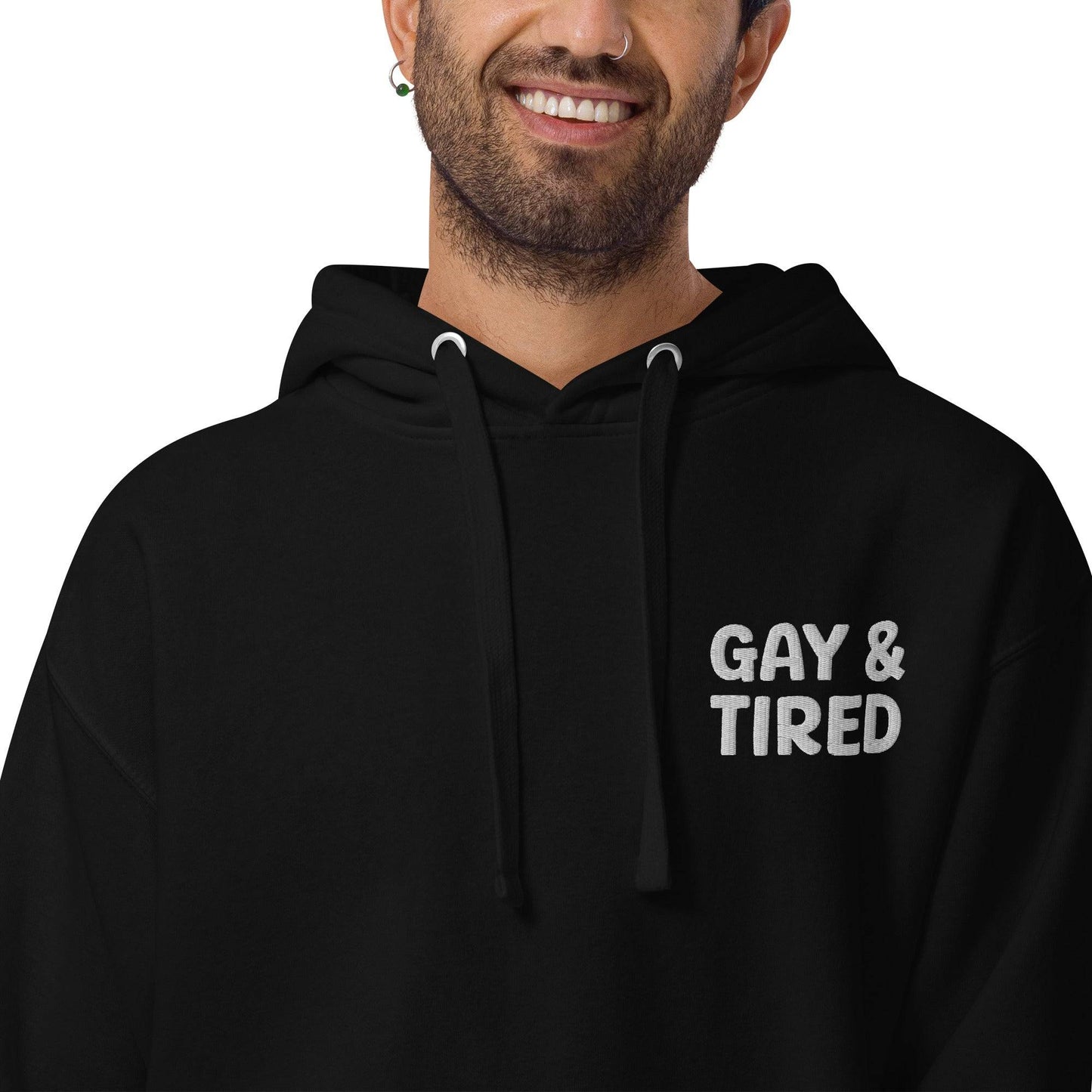 The Gay & Tired Hoodie by Pridelity is a black pride hoodie featuring white text on the upper left side that reads "GAY & TIRED." It comes with a front pocket and drawstrings for the hood.