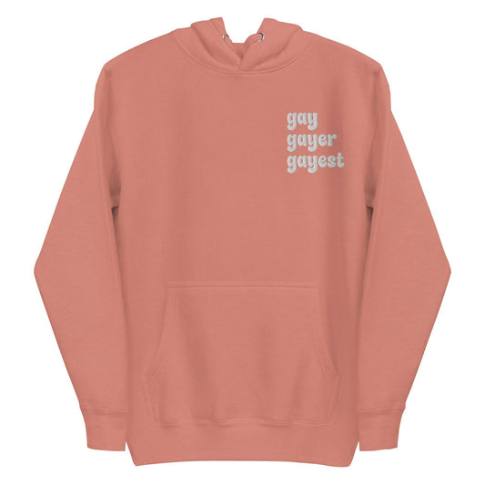 A Dusty Rose-colored hoodie from Pridelity's collection, named "Gay Gayer Gayest Hoodie," features a front pocket and the text "gay gayer gayest" printed in white on the upper left side.