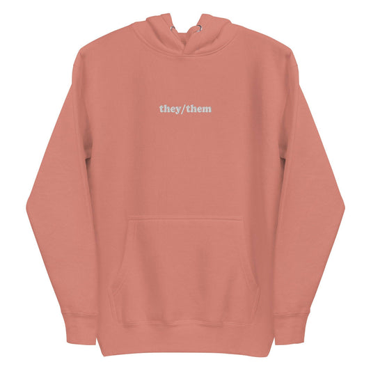 Introducing the They/Them Hoodie from Pridelity's pride collection. This LGBTQ+ friendly piece comes in a folded dusty rose color and features "they/them" text in white on the front. Complete with a drawstring, it offers a soft, casual appearance.