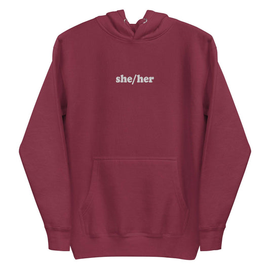 Introducing the She/Her Hoodie from Pridelity's pride collection, crafted in a maroon hue and adorned with "she/her" text in white on the chest. This hoodie features a front pocket and drawstrings at the hood, providing a straightforward and casual style ideal for promoting LGBTQ+ visibility.