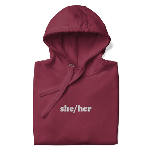 Introducing the She/Her Hoodie from Pridelity's pride collection, crafted in a maroon hue and adorned with "she/her" text in white on the chest. This hoodie features a front pocket and drawstrings at the hood, providing a straightforward and casual style ideal for promoting LGBTQ+ visibility.