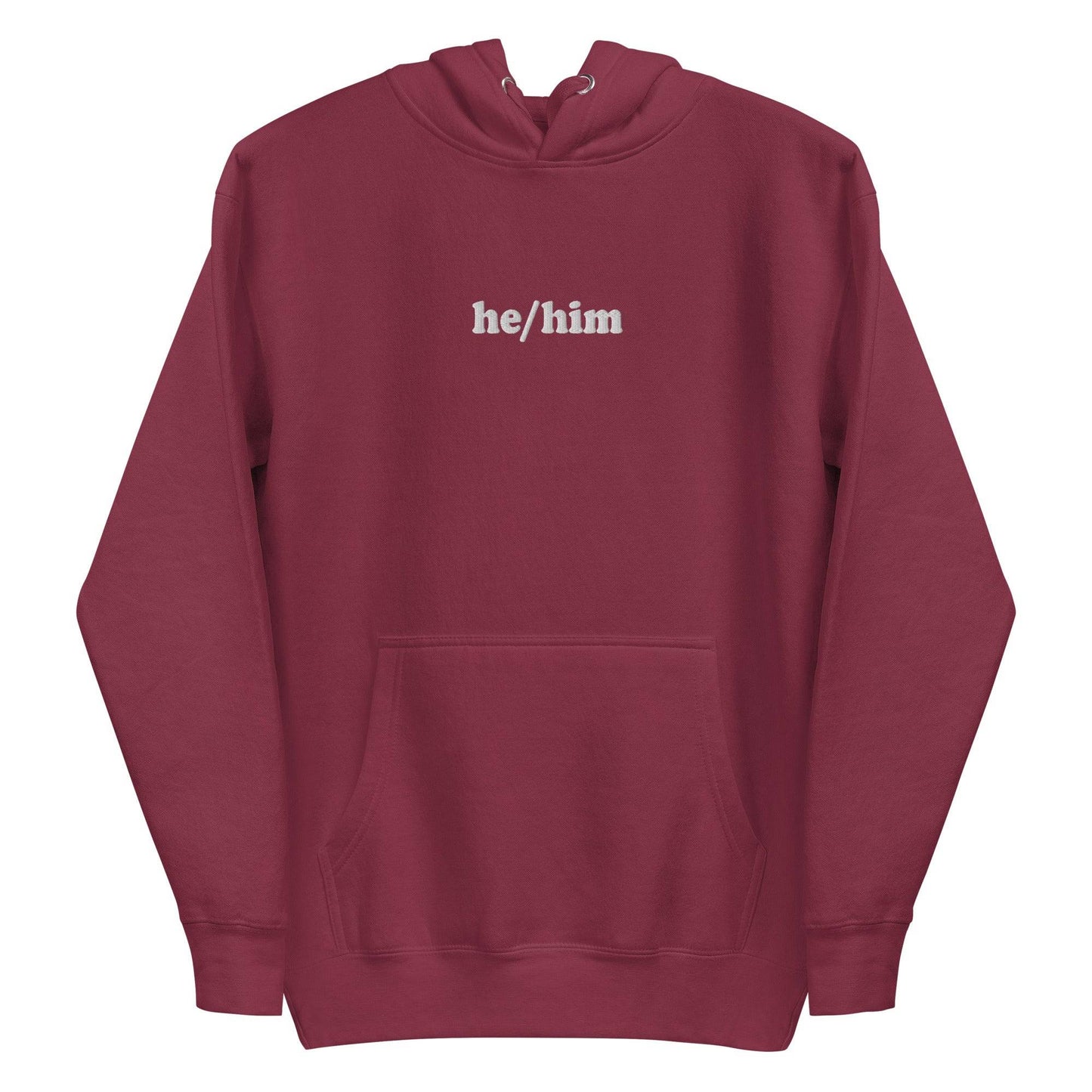 A neatly folded Pridelity He/Him Hoodie in black, featuring the text "he/him" embroidered in white on the front. The hood is showcased with its drawstrings arranged against a plain white background.