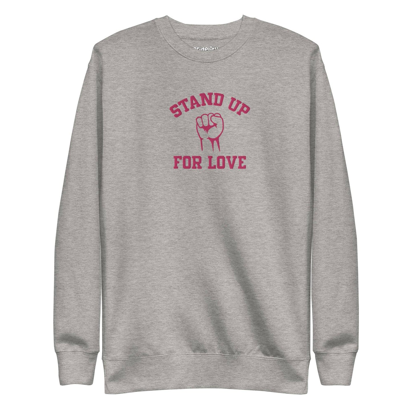 A folded white Pridelity Stand Up Sweatshirt showcases the phrase "STAND UP FOR LOVE" in red, encircling a striking graphic of a raised fist, making it a distinctive addition to any pride collection.