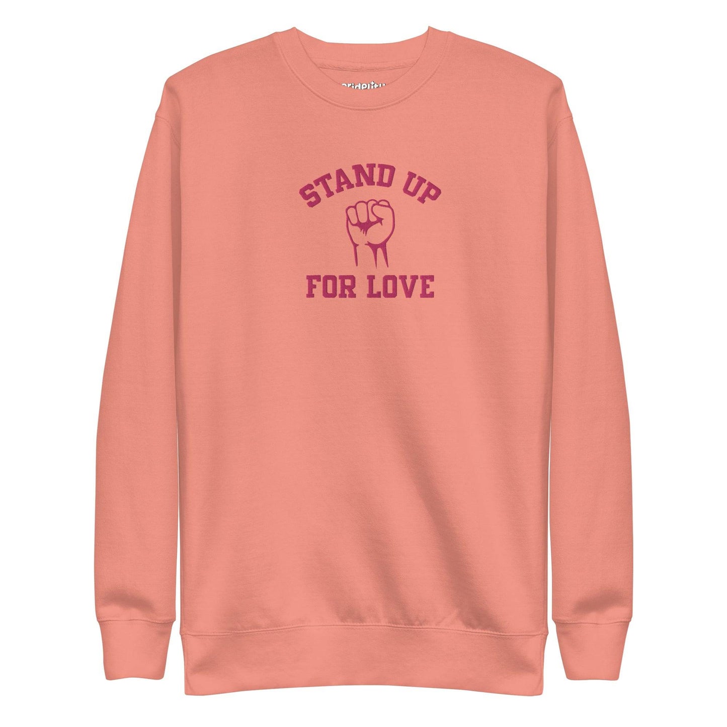 A folded white Pridelity Stand Up Sweatshirt showcases the phrase "STAND UP FOR LOVE" in red, encircling a striking graphic of a raised fist, making it a distinctive addition to any pride collection.