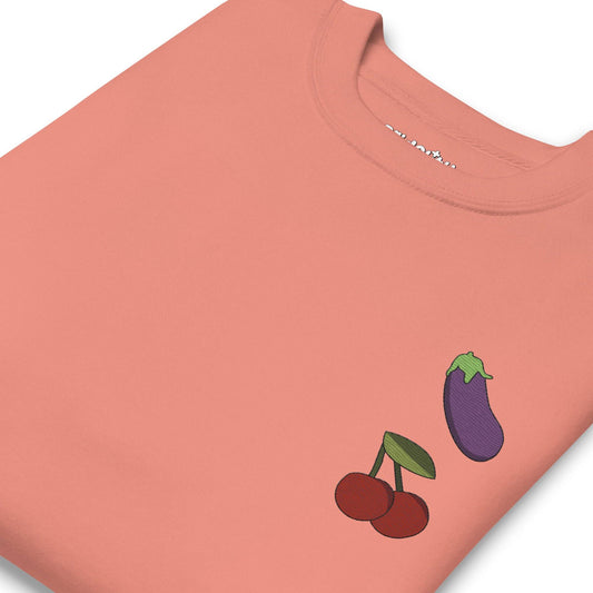 Check out the "Yummy Emojis Sweatshirt" by Pridelity in a dusty rose hue, showcasing small embroidered designs of an eggplant and cherries on the upper left side. This sweatshirt, from our exclusive pride collection, features a classic crew neck and long sleeves, making it perfect for any pride ensemble.