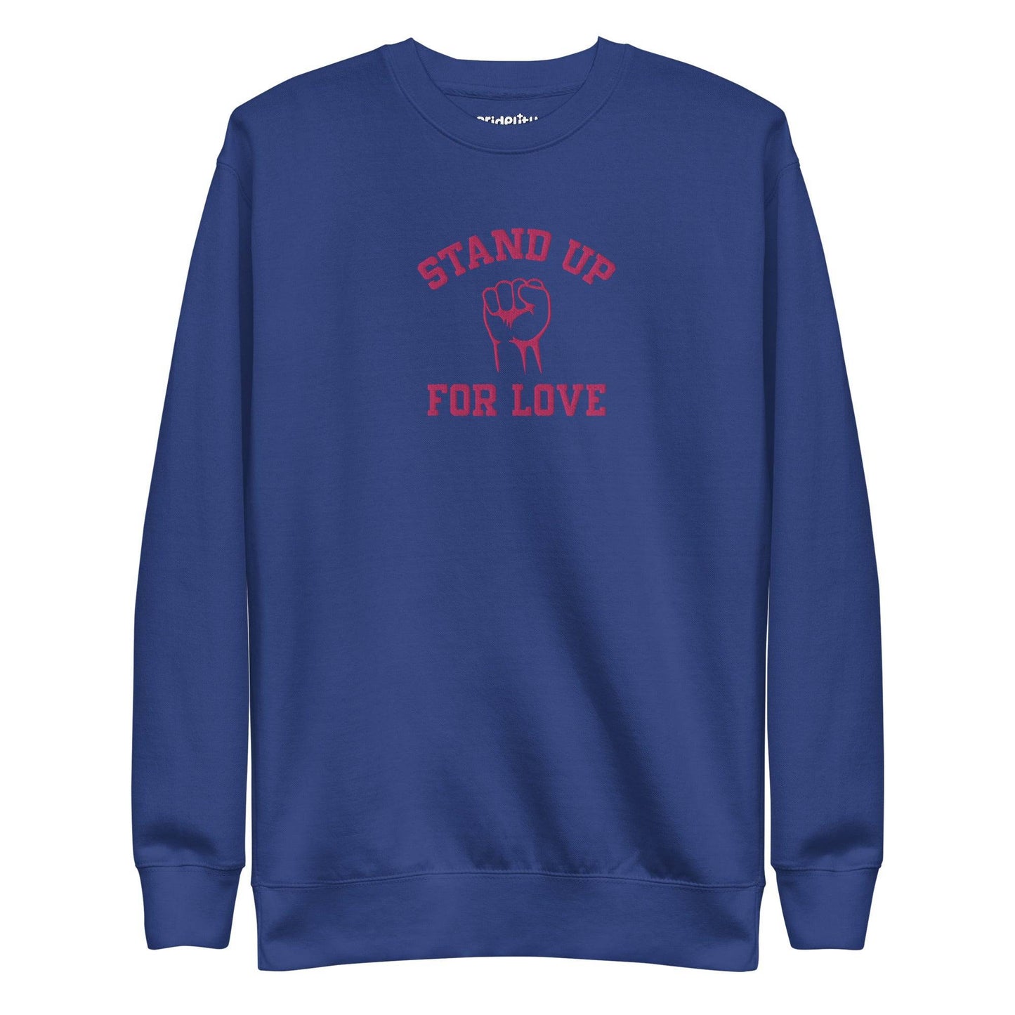 A folded white Pridelity Stand Up Sweatshirt showcases the phrase "STAND UP FOR LOVE" in red, encircling a striking graphic of a raised fist, making it a distinctive addition to any pride collection.