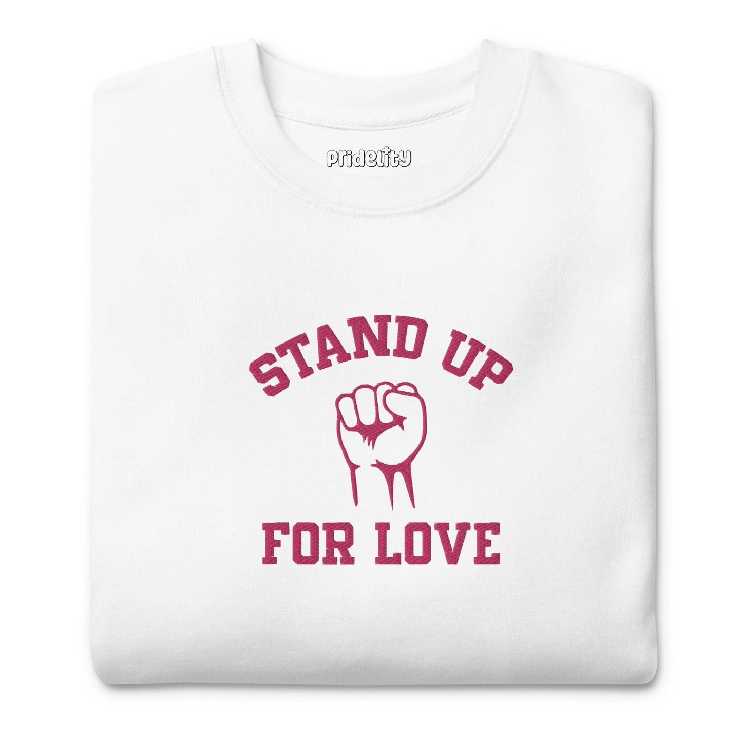 A folded white Pridelity Stand Up Sweatshirt showcases the phrase "STAND UP FOR LOVE" in red, encircling a striking graphic of a raised fist, making it a distinctive addition to any pride collection.
