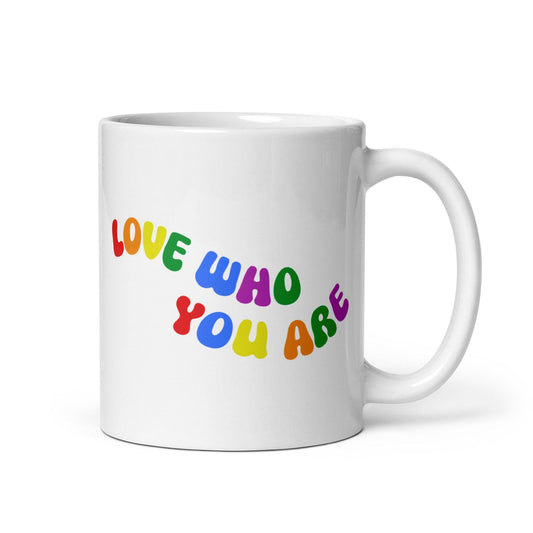 The Love Who You Are Mug by Pridelity is a white mug featuring vibrant letters spelling "LOVE WHO YOU ARE" on its side. It has a smooth handle and a simple background, and is part of the Pride Collections 2025, celebrating uniqueness and self-love.