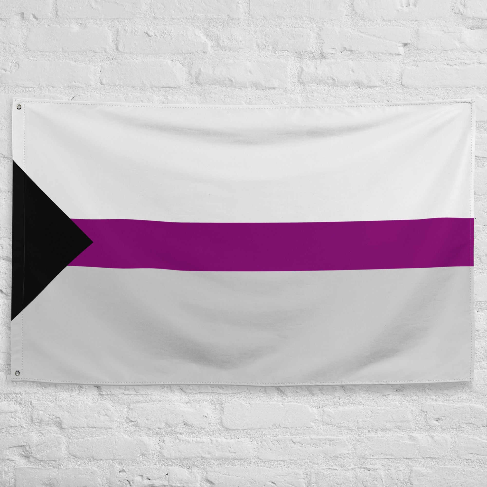 The Demisexual Pride Flag from Pridelity features a design with a black triangle on the left, white stripes, a wide purple band in the center, followed by another white stripe. It is beautifully displayed against a white brick wall.