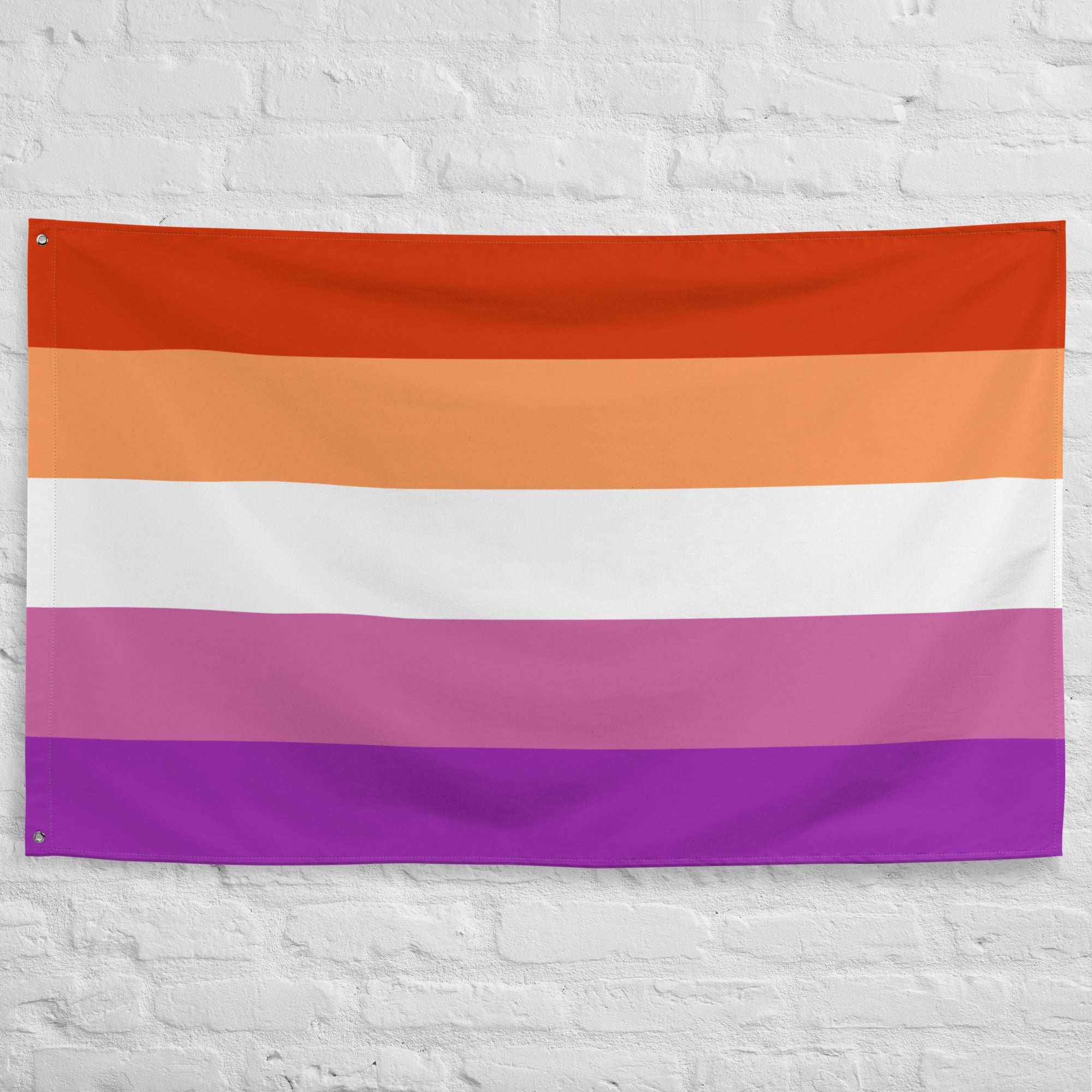 A Pridelity Lesbian Pride Flag with horizontal stripes in dark orange, orange, light orange, white, pink, and purple hung on a white brick wall outside the Rainbow Shop.