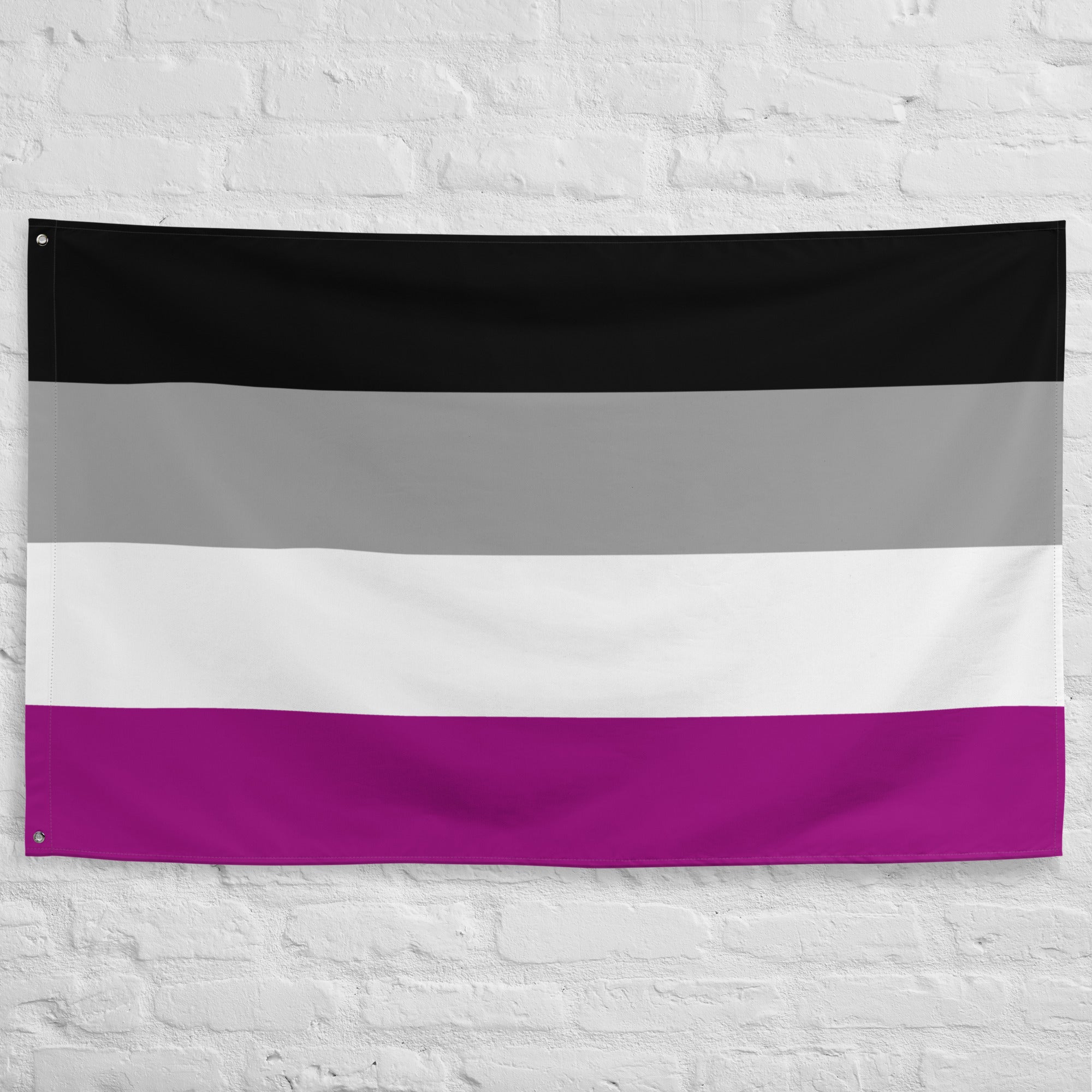 The image showcases the Asexual Pride Flag by Pridelity, part of the Pride Collections, hanging against a white brick wall. The flag features four horizontal stripes in black, gray, white, and purple.