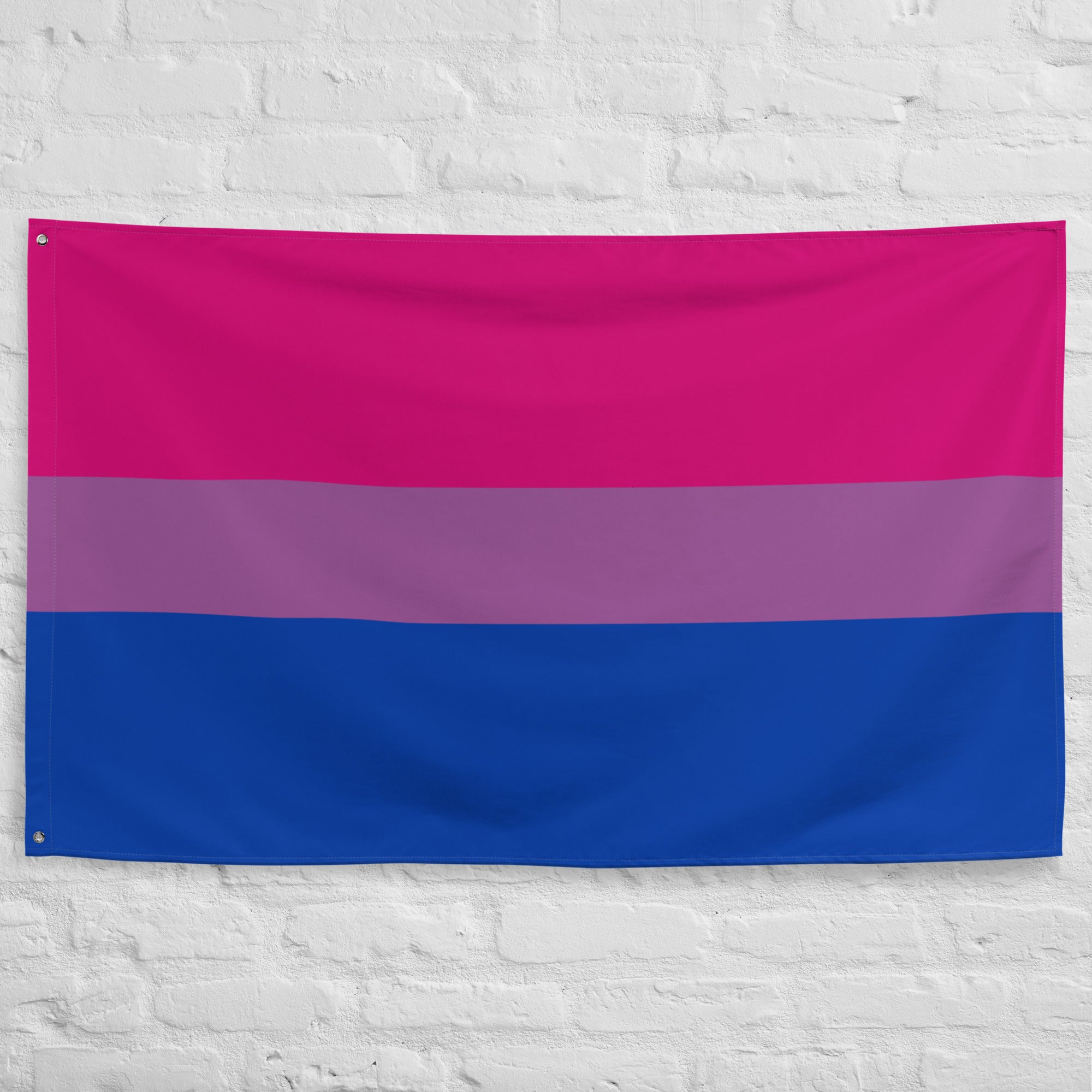 The Bisexual Pride Flag from Pridelity boasts horizontal stripes with a vibrant design: a bright pink on top, a thin purple in the middle, and a deep blue at the bottom. Displayed elegantly against a white brick wall, it embodies the spirit of Pride.