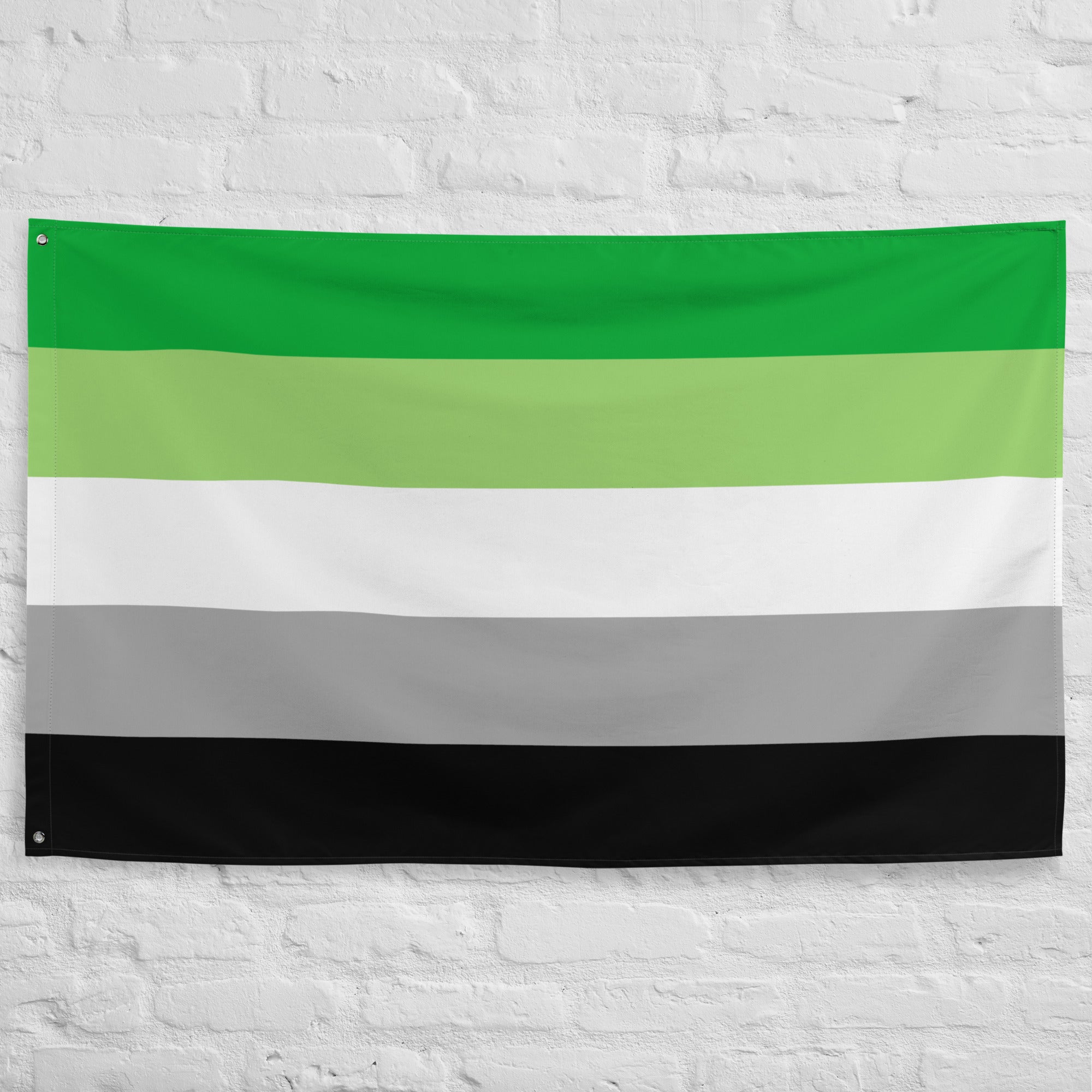 Image of Pridelity’s Aromantic Pride Flag hanging on a white brick wall, showcasing the vibrant colors of dark green, light green, white, gray, and black. This striking piece is part of our exclusive Pride Collections.